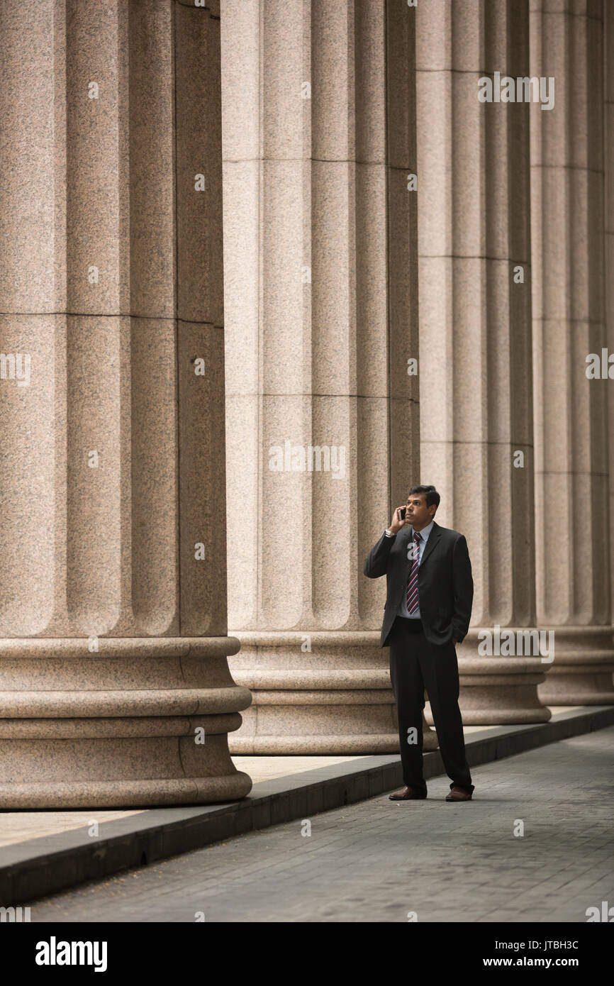 Homme d'affaires indien ou d'un avocat à l'aide d'un téléphone intelligent à l'extérieur d'un édifice du palais colonial. Banque D'Images