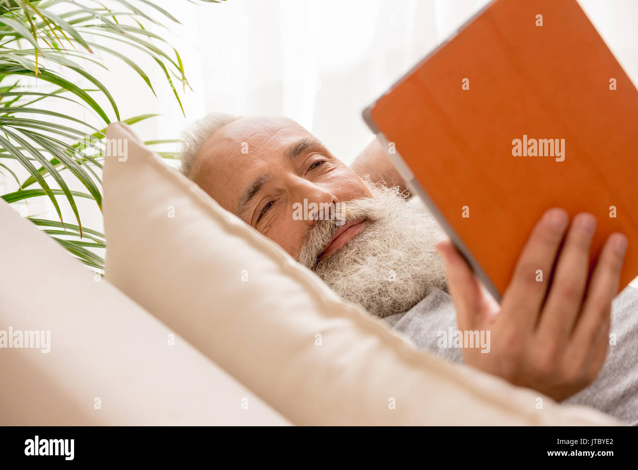 Happy bearded man using digital tablet et lying on sofa at home Banque D'Images