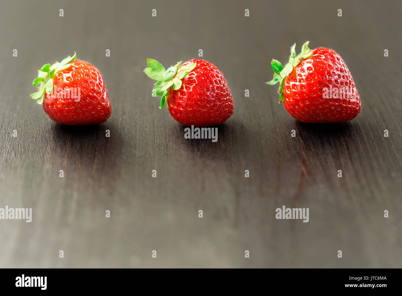 Trois baies rouges de fraises fraîches sur une table en bois noir Banque D'Images