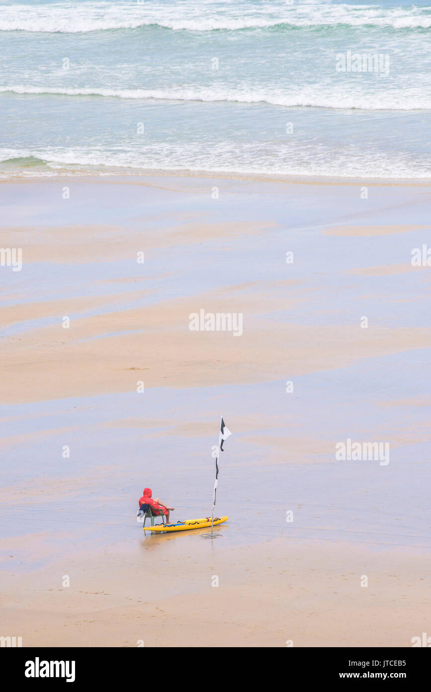 Un sauveteur RNLI en service sur une paisible plage déserte à Newquay, Cornwall. Banque D'Images