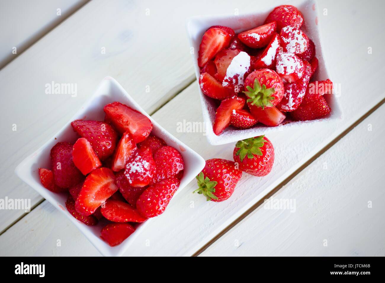 Vue du haut vers le bas de deux carrés blanc chine bols de couper les fraises avec du sucre en poudre sur la table en bois Banque D'Images