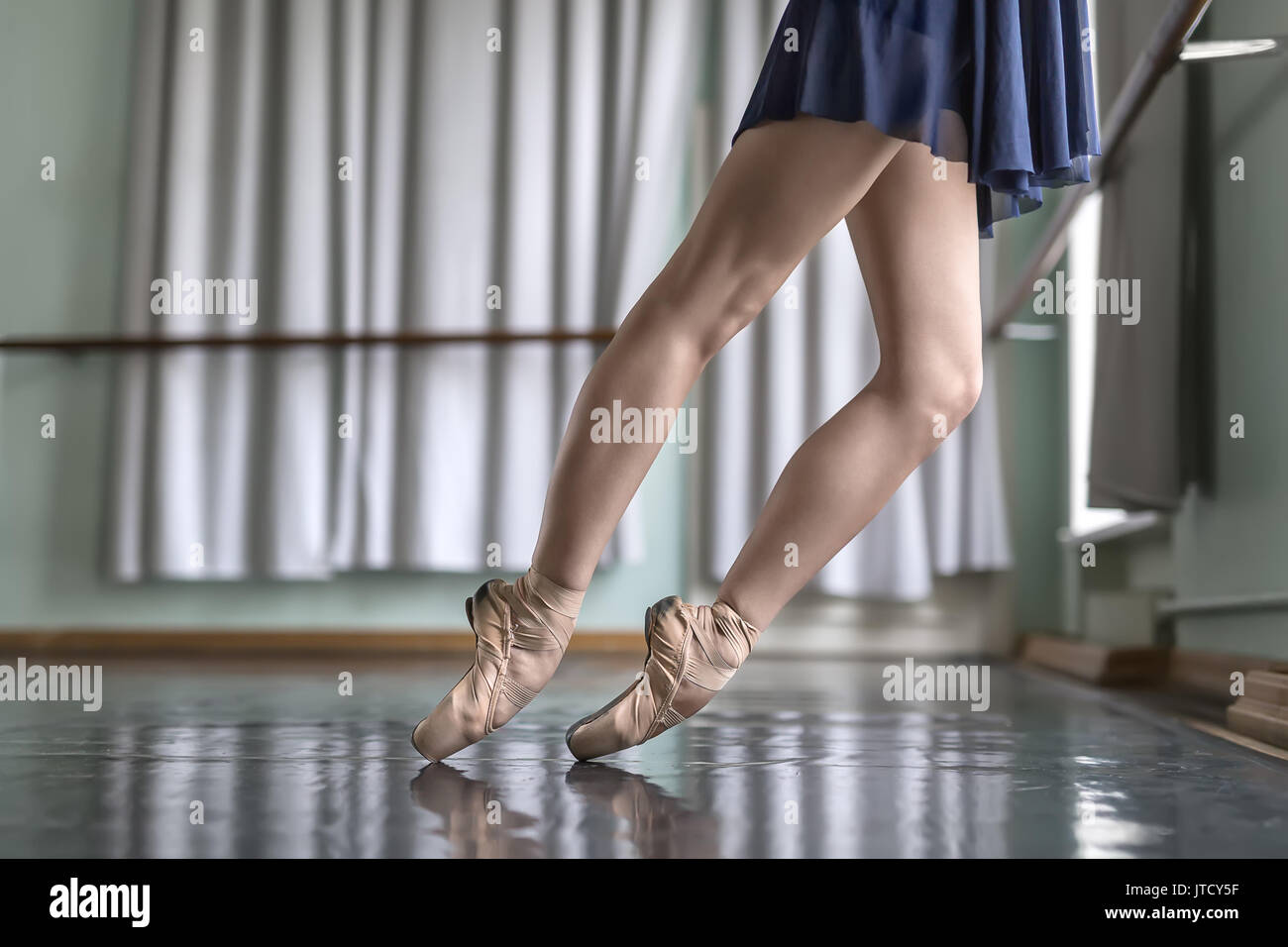 Les jambes d'un danseur de ballet dans un bleu vêtements de danse qui se tient sur pointes à côté de la barre de ballet. Elle porte des chaussures pointe beige. Ses pieds reflète dans la g Banque D'Images