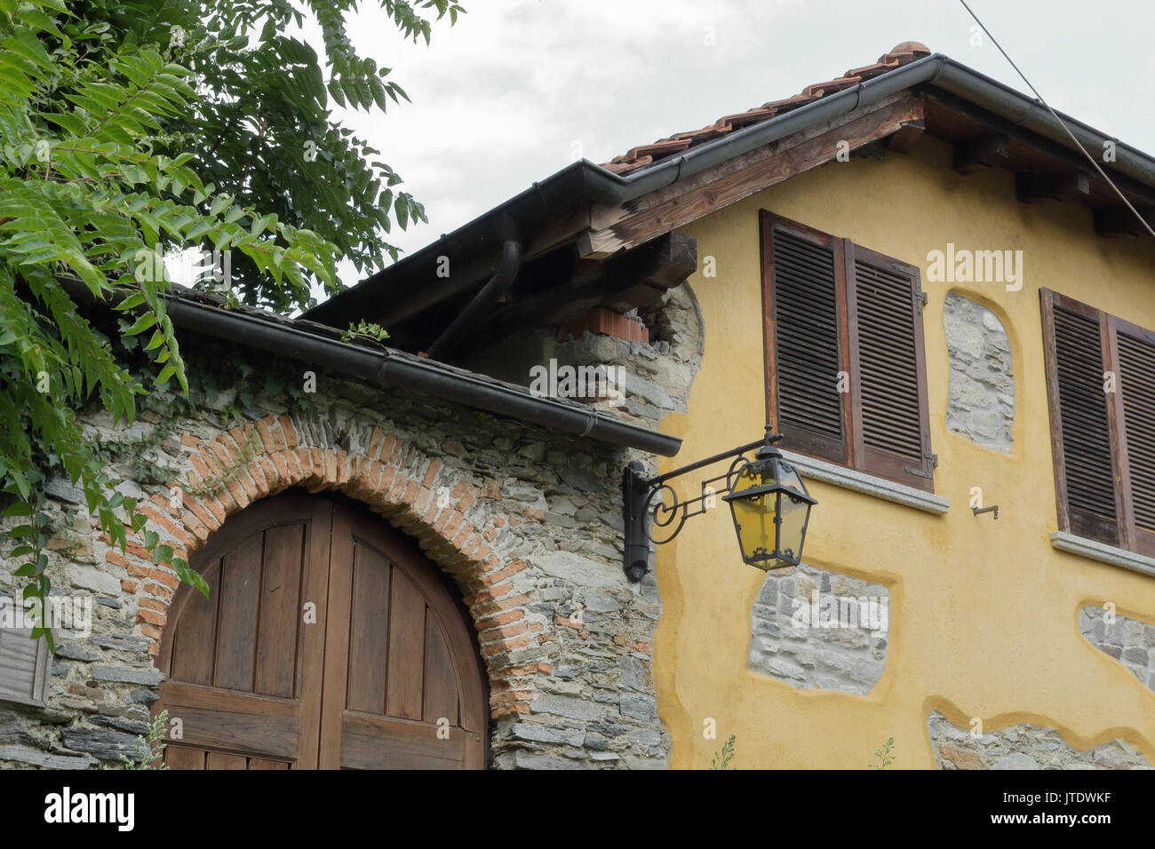 Une campagne maison en pierre jaune avec deux fenêtres avec volets, une porte avant en bois à côté d'un arbre et une lanterne de rue Banque D'Images