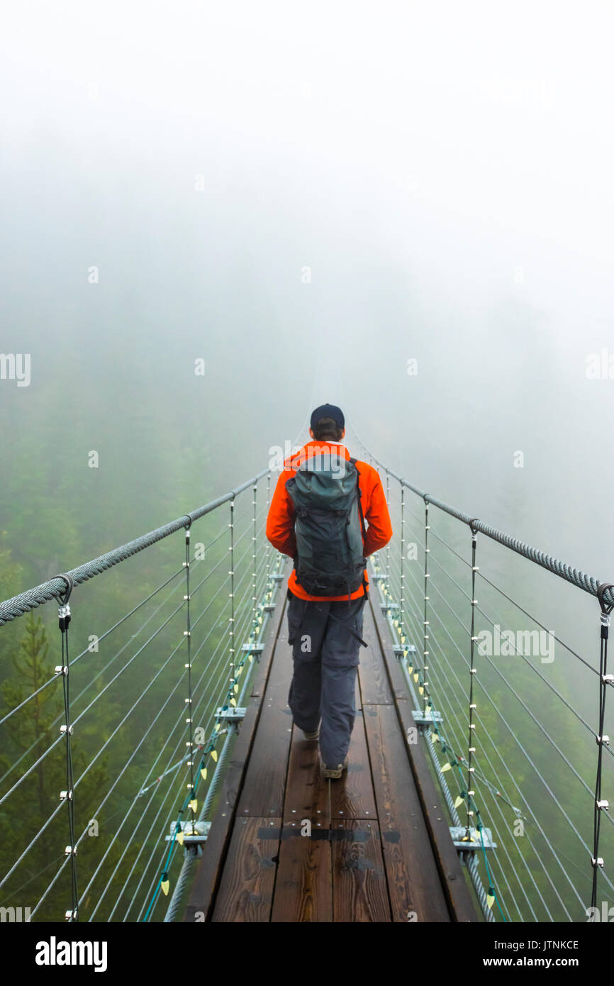 Un homme marche sur un pont suspendu sur un jour d'automne pluvieux à Squamish, en Colombie-Britannique. Banque D'Images