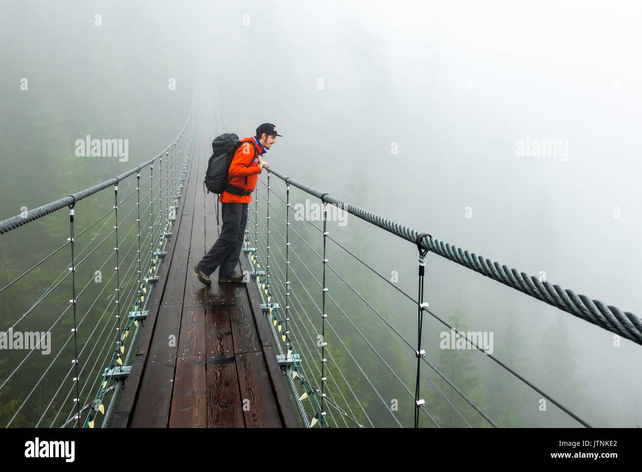 Un homme regarde au-dessus d'un pont suspendu sur un jour d'automne pluvieux à Squamish, en Colombie-Britannique. Banque D'Images