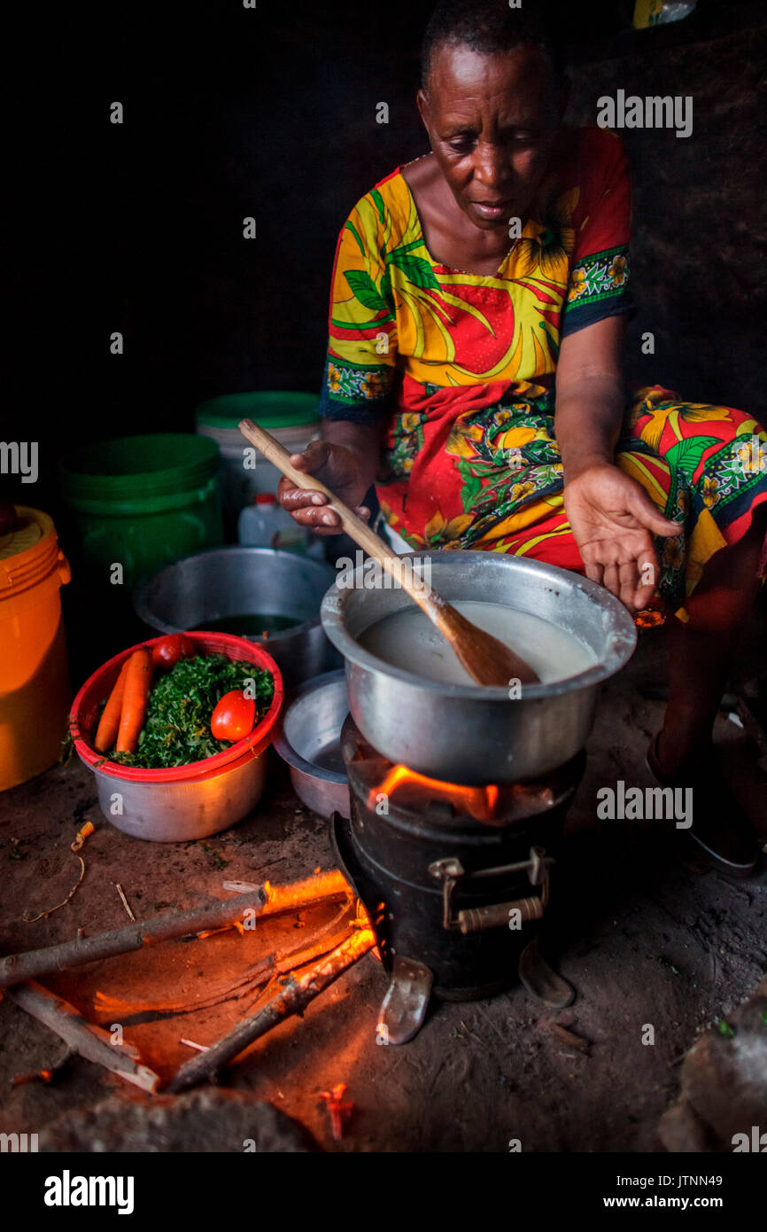 Chez elle, près d'Arusha, en Tanzanie, Julieth Mollel, sœur de Solar, prépare un dîner d'ugali, de légumes et de haricots sur sa cuisinière propre. L'ugali est un aliment de base consommé dans de nombreux pays d'Afrique et est de la bouillie de farine de maïs. travailler dans sa cuisine extérieure compacte la nuit est plus facile maintenant avec la cuisinière propre qui émet très peu de fumée et utilise seulement une fraction du bois de chauffage d'une cuisinière traditionnelle à trois pierres. Banque D'Images