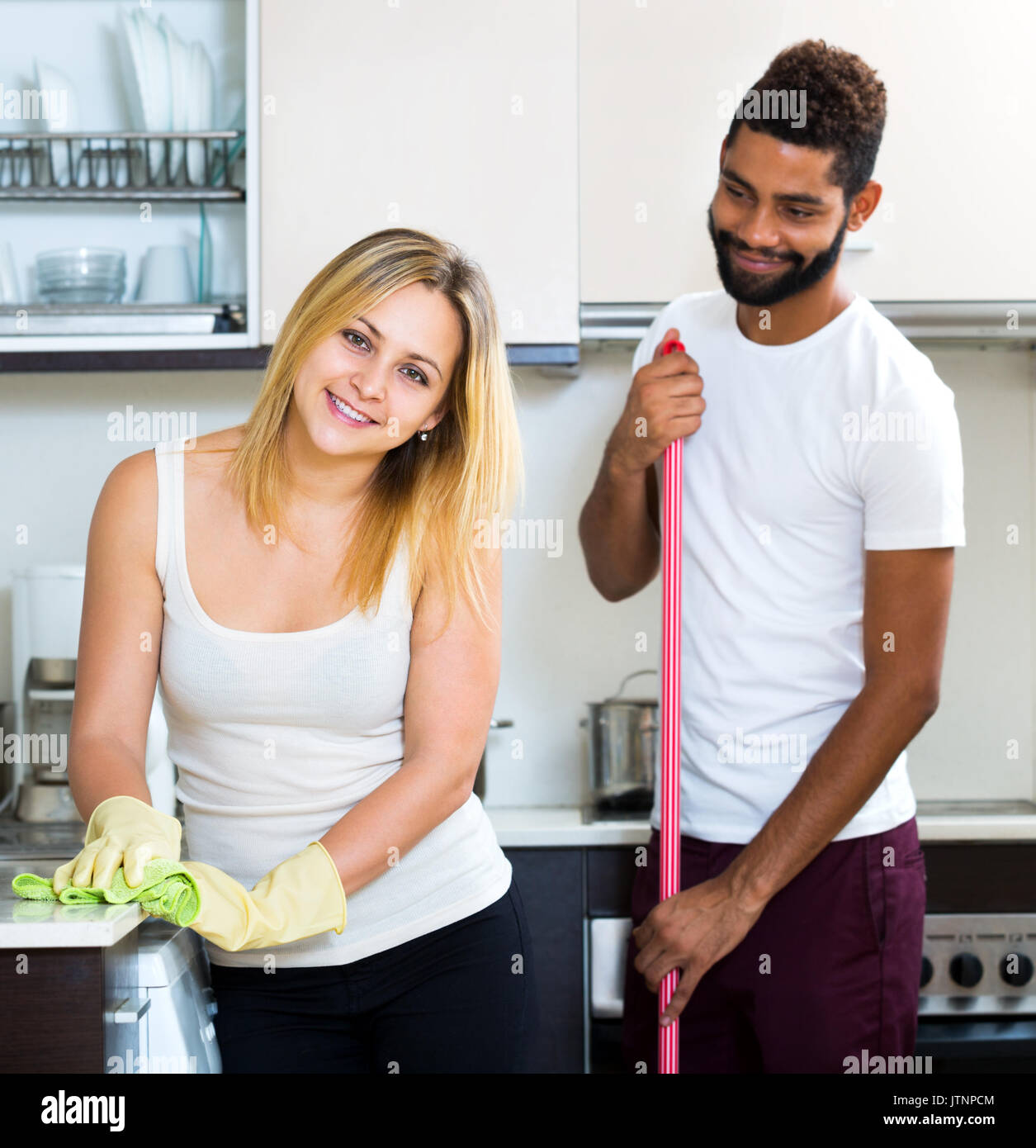 Mari Noir avec blanc smiling young woman dusting dans cuisine domestique Banque D'Images