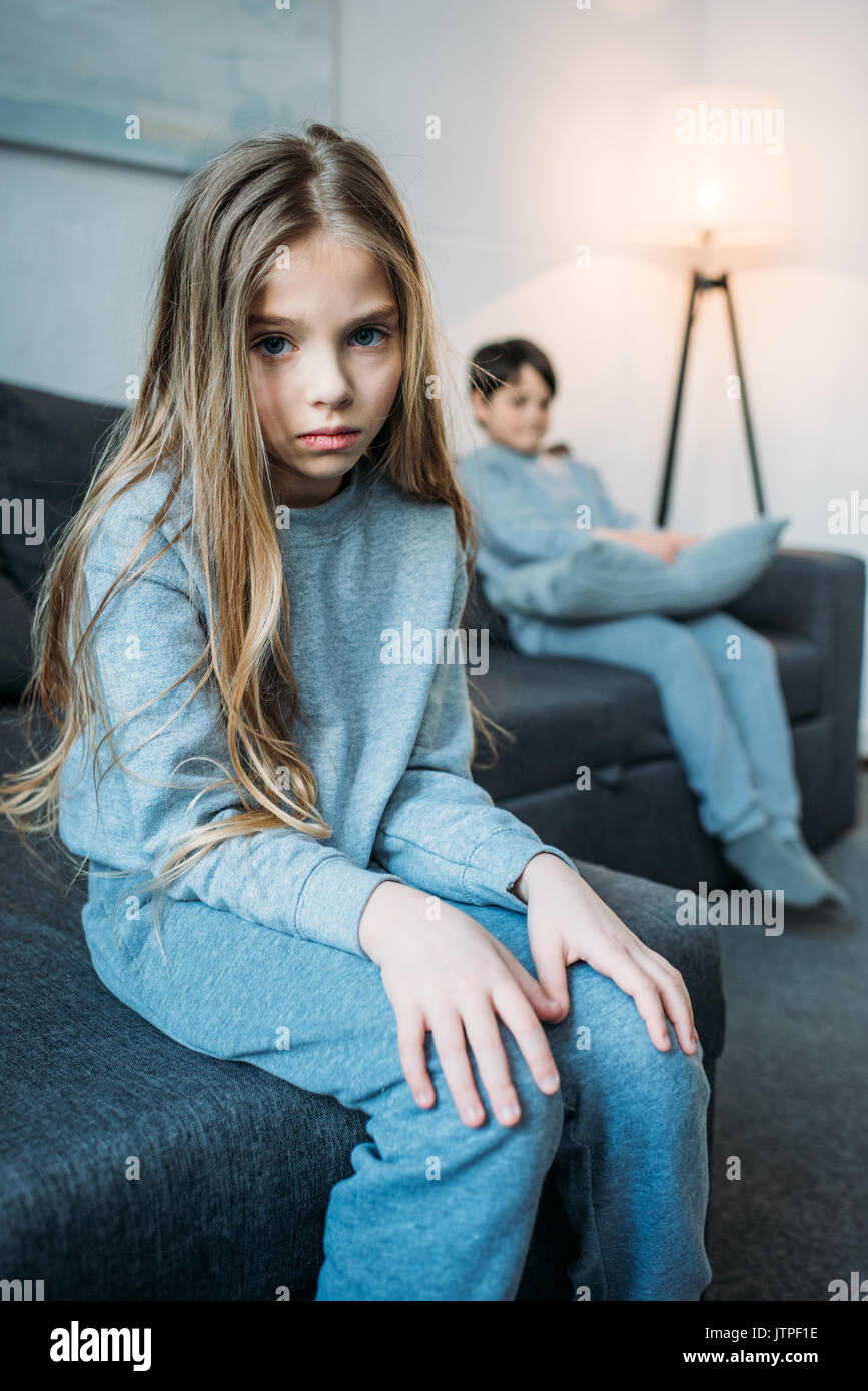 Bouleversée petite fille en pyjama à la caméra à tout petit frère assis derrière Banque D'Images