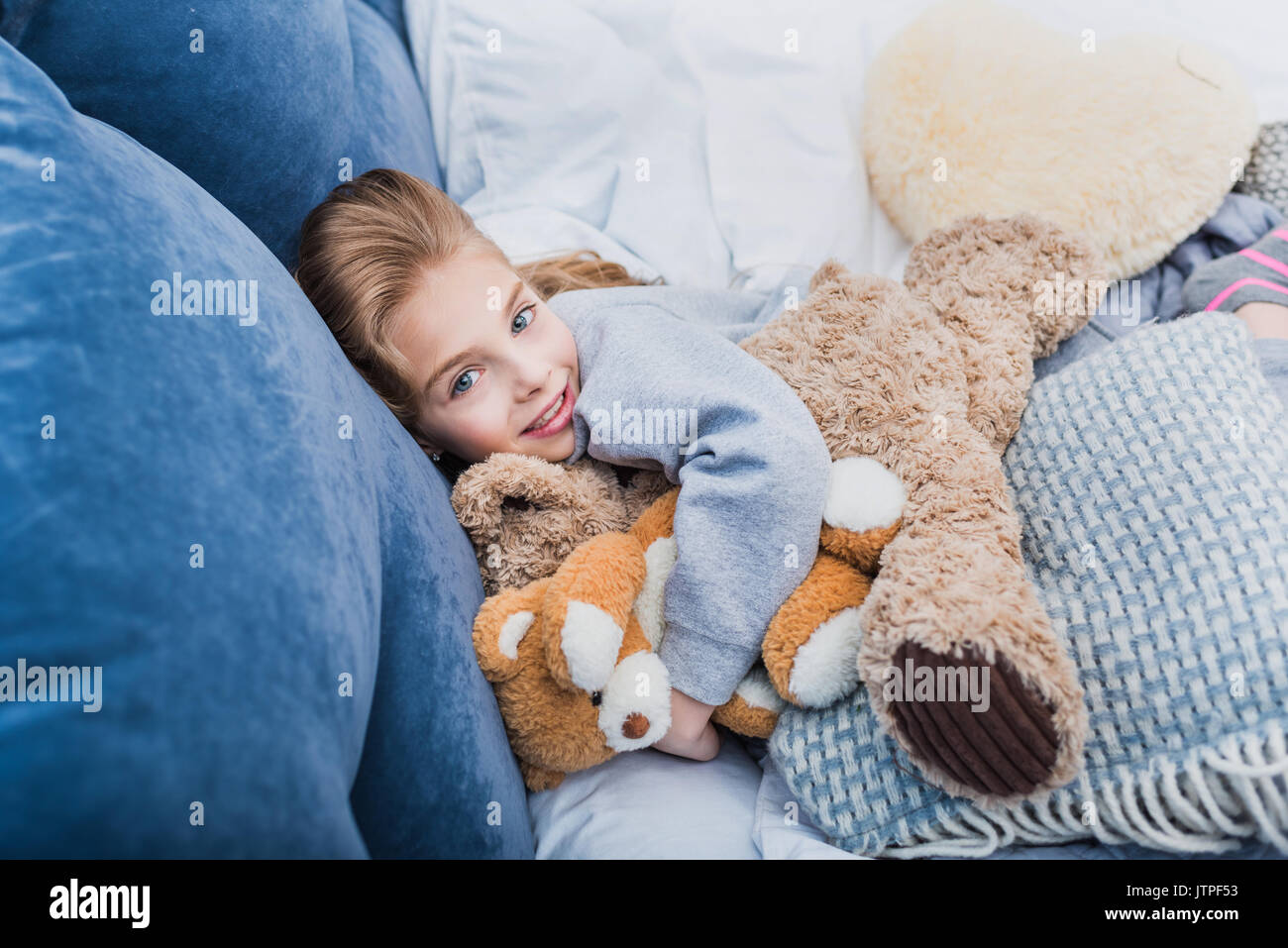 Adorable petite fille lying on bed with teddy bears and smiling at camera Banque D'Images