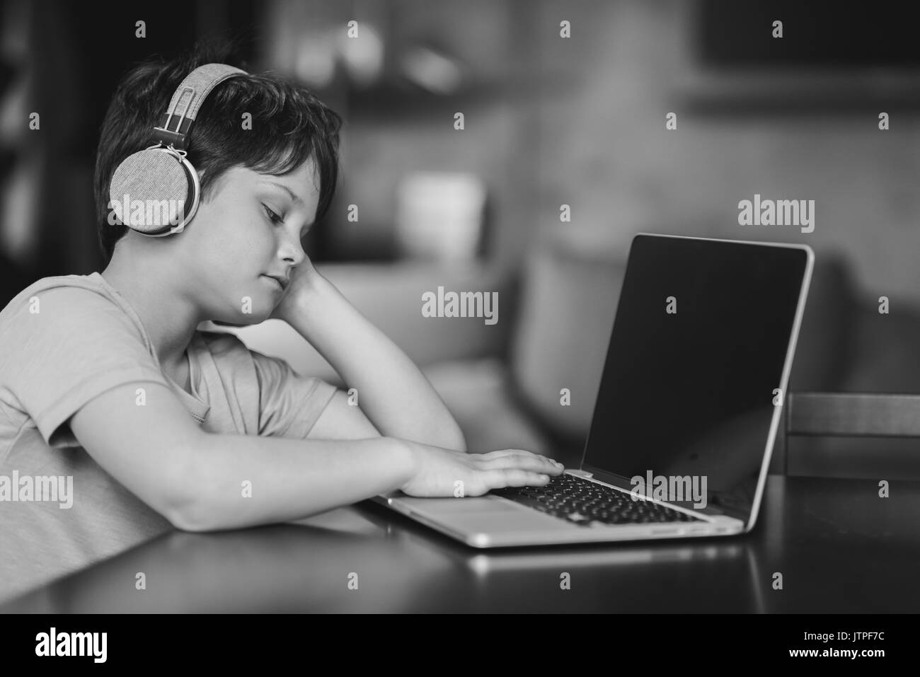 Kid garçon écoutant de la musique dans le casque tout en restant assis à la maison et de la saisie sur ordinateur portable, noir et blanc Banque D'Images