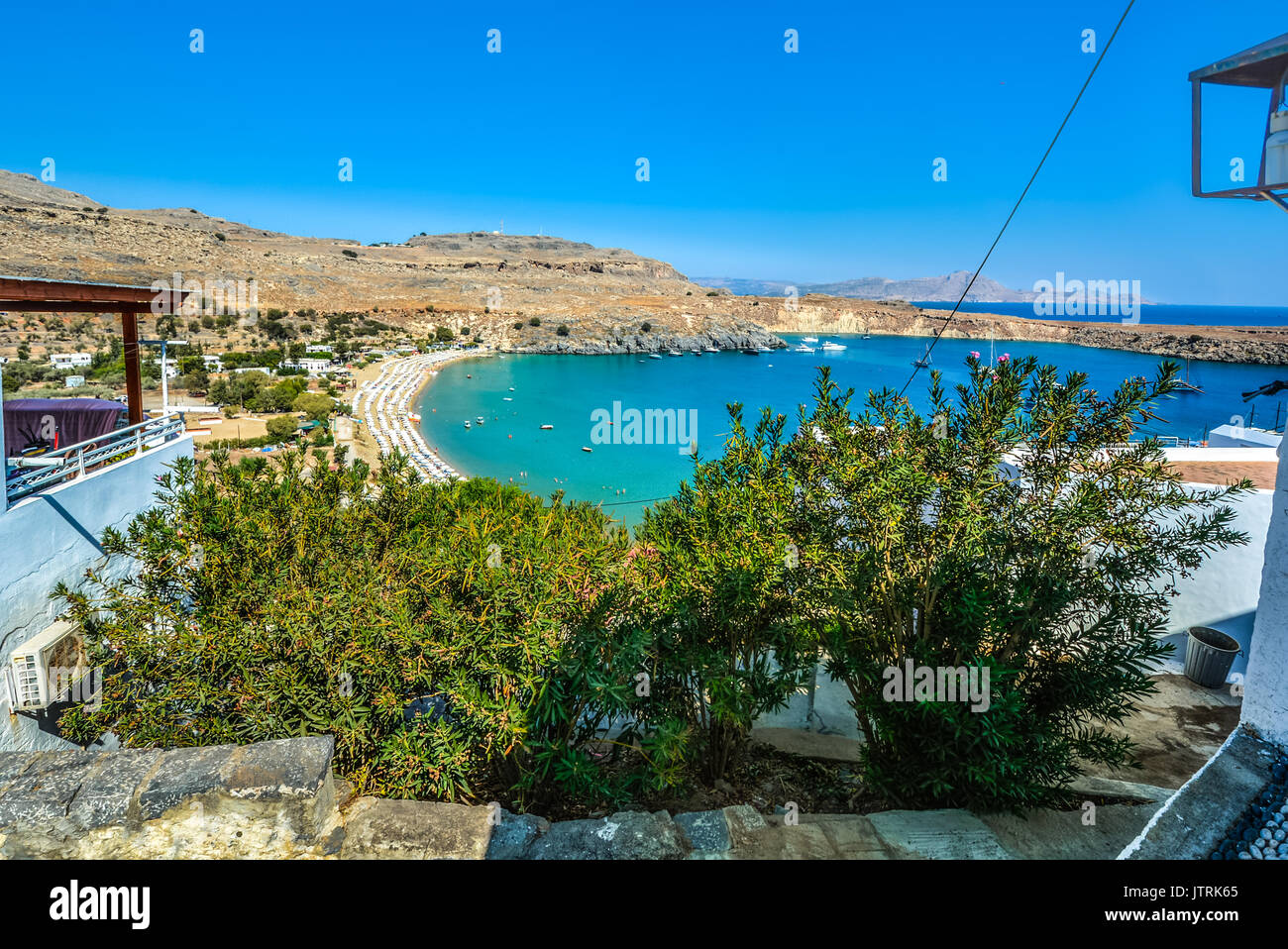 Petite baie de Lindos sur l'île de Rhodes Grèce encombré avec des parasols, des bateaux et des nageurs profitez de la baie et de la mer Méditerranée sur une chaude journée Banque D'Images