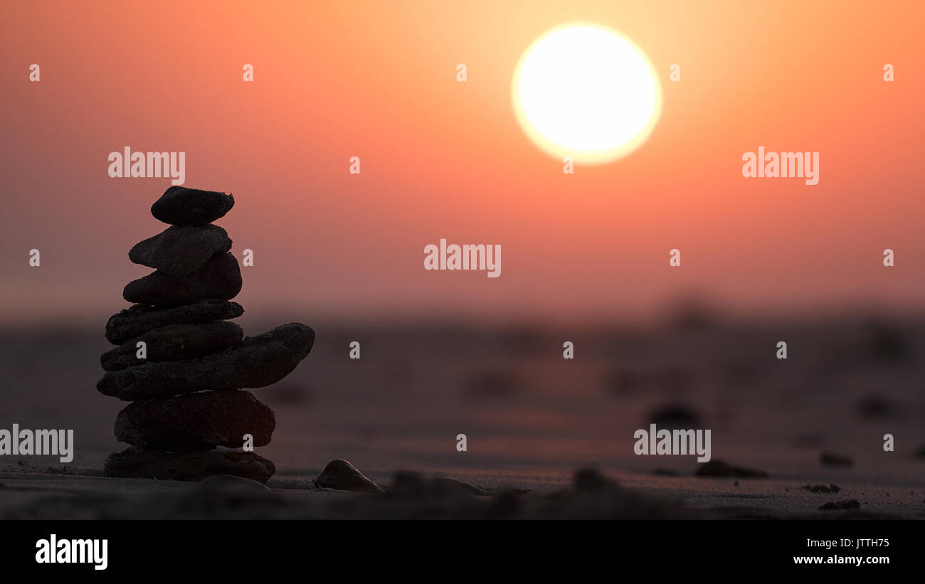 - L'équilibre des pierres empilées sur une plage contre un coucher de soleil orange avec ciel rosâtre à Mandvi Kachchh Inde Banque D'Images