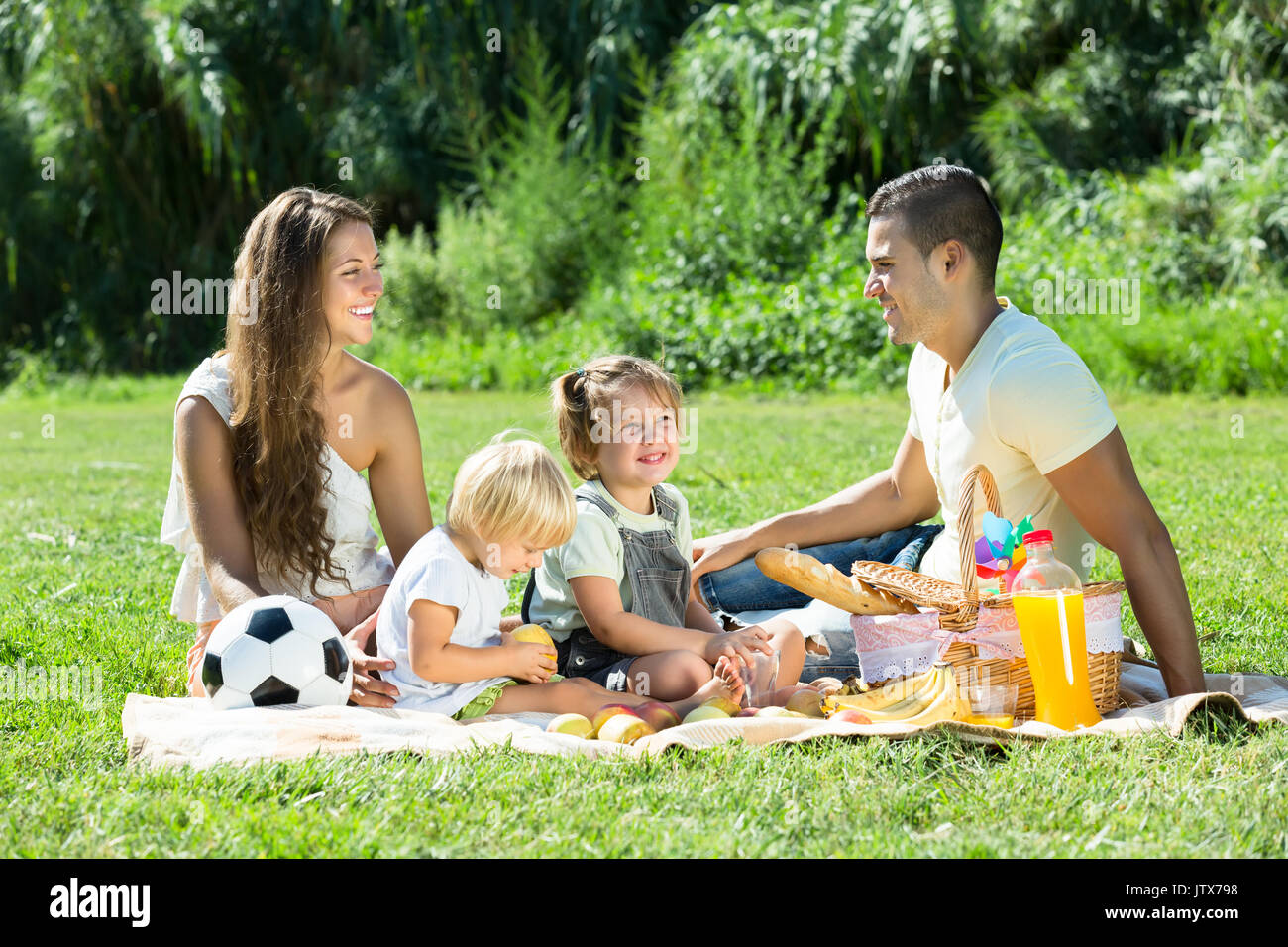 Young smiling family de quatre having picnic à meadow au jour d'été Banque D'Images