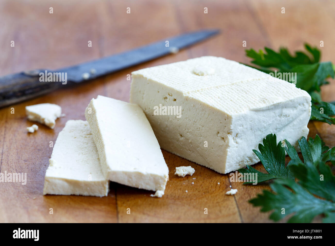 Un bloc de tofu blanc avec deux tranches de tofu, grillée, persil frais et couteau rustique en bois sur planche à découper. Banque D'Images