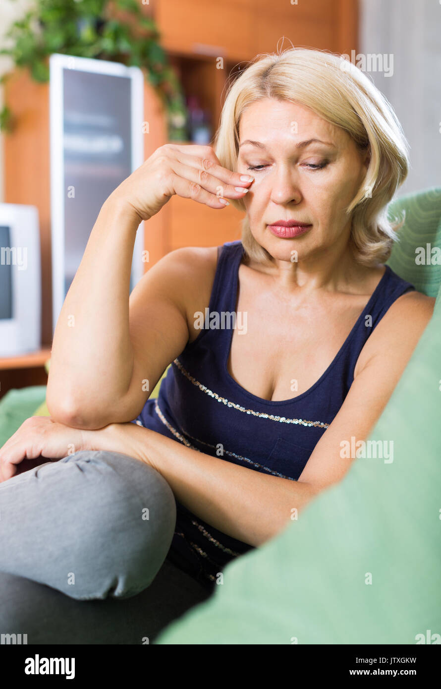 Triste et solitaire mature femme assise sur la table à la maison Banque D'Images