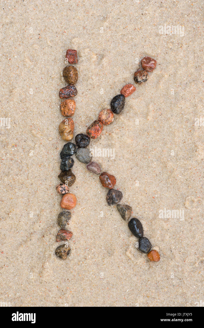 Lettre k de galets sur fond de sable Banque D'Images