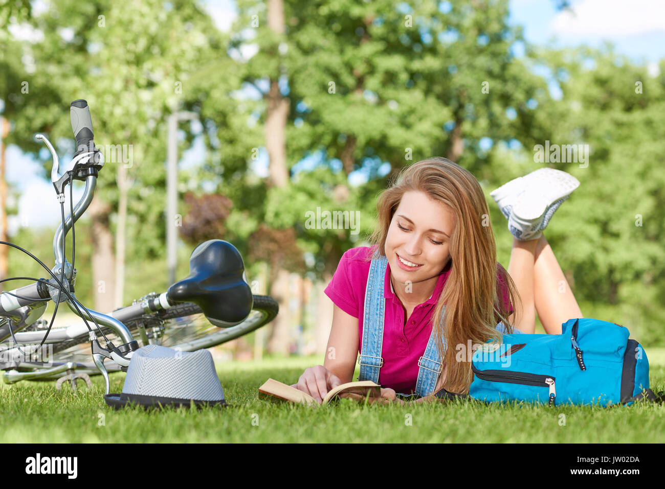 Magnifique jeune femme heureuse sourire en lisant un livre de détente sur l'herbe après le vélo dans le parc de loisirs vacances de printemps de l'été bonheur li Banque D'Images