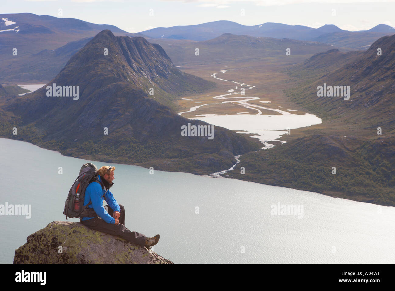 Un randonneur jouit de la vue sur les fjords et les montagnes tout en étant assis sur un rocher de la fameuse crête de Besseggen en Norvège. Cette traverse un jour dans le parc national de Jotunheimen est le sentier de randonnée le plus populaire en Norvège. Banque D'Images