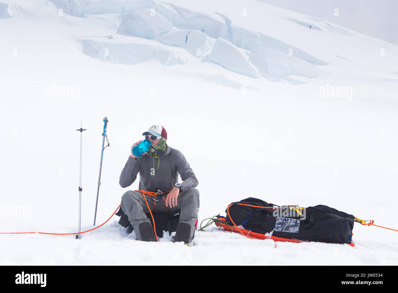 Un ski est au repos et de l'eau potable tout en restant assis sur son sac à dos sur le glacier de Kahiltna Parc National Denali en Alaska. Banque D'Images