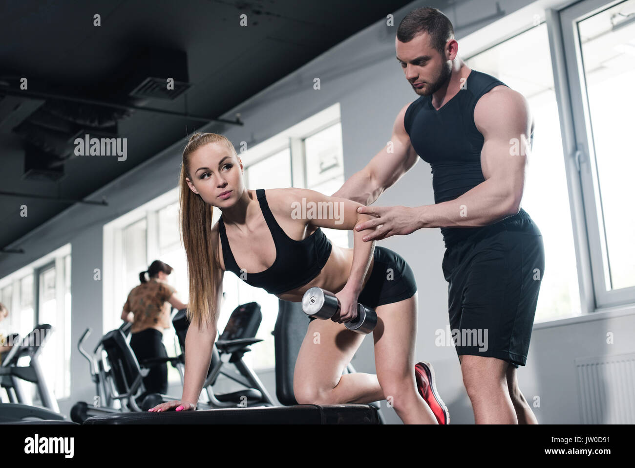 Aider l'instructeur young woman exercising with dumbbell at gym Banque D'Images