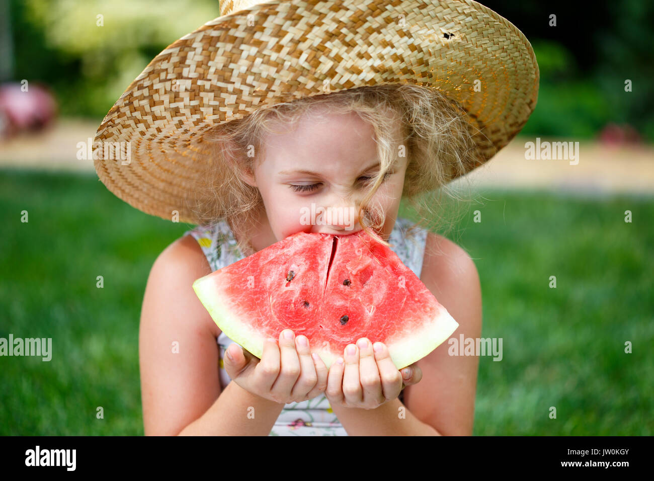 Petite fille au chapeau de paille avec de grandes tranche de pastèque assis sur l'herbe verte en été park Banque D'Images