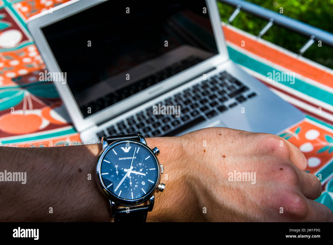 Vue depuis les yeux. Contrôle de l'heure sur un Giorgio Armani avec un ordinateur portable portant sur une chaise longue à l'arrière-plan. Banque D'Images