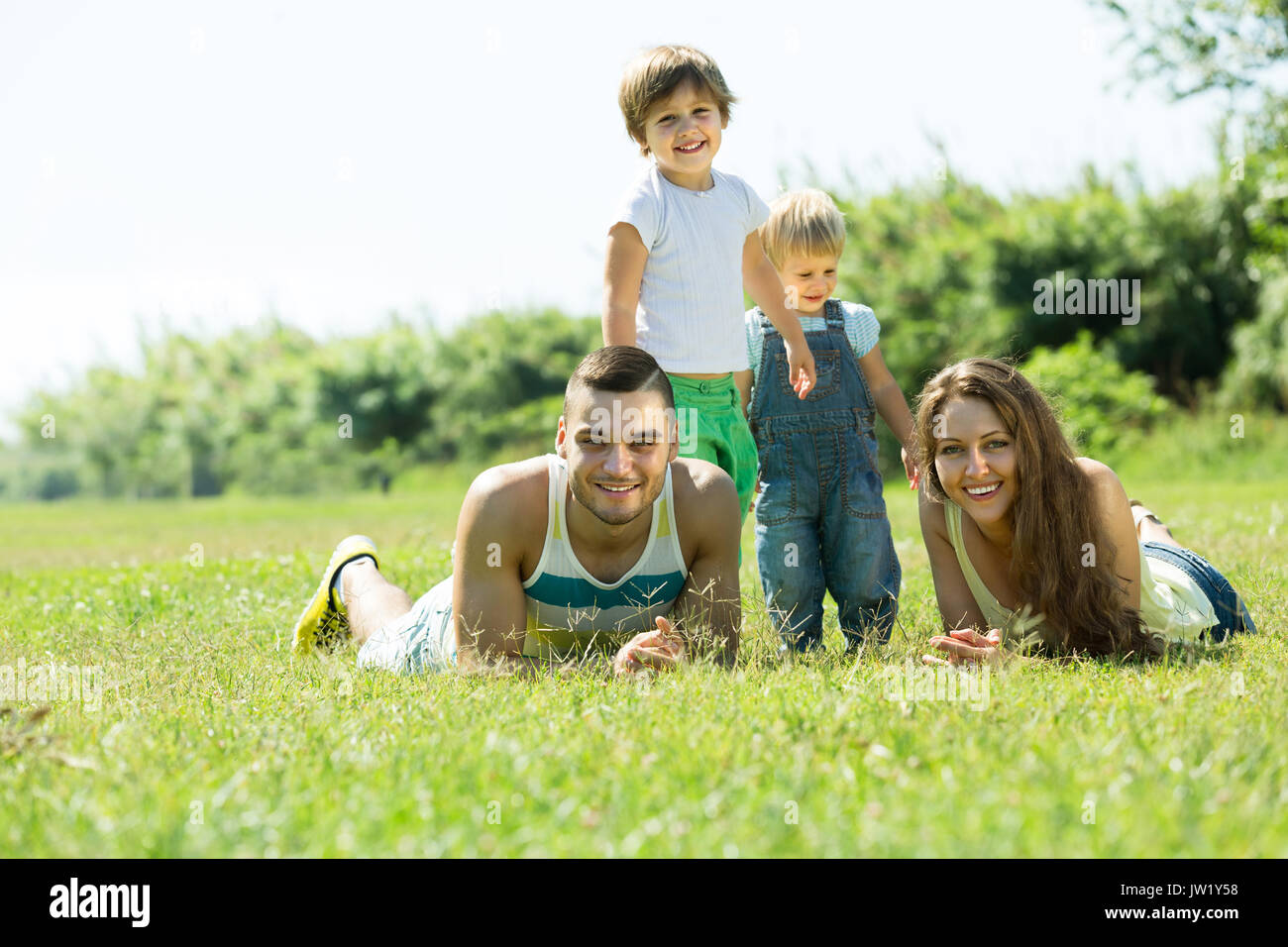 Heureuse famille des quatre lying on grass in sunny summer park Banque D'Images