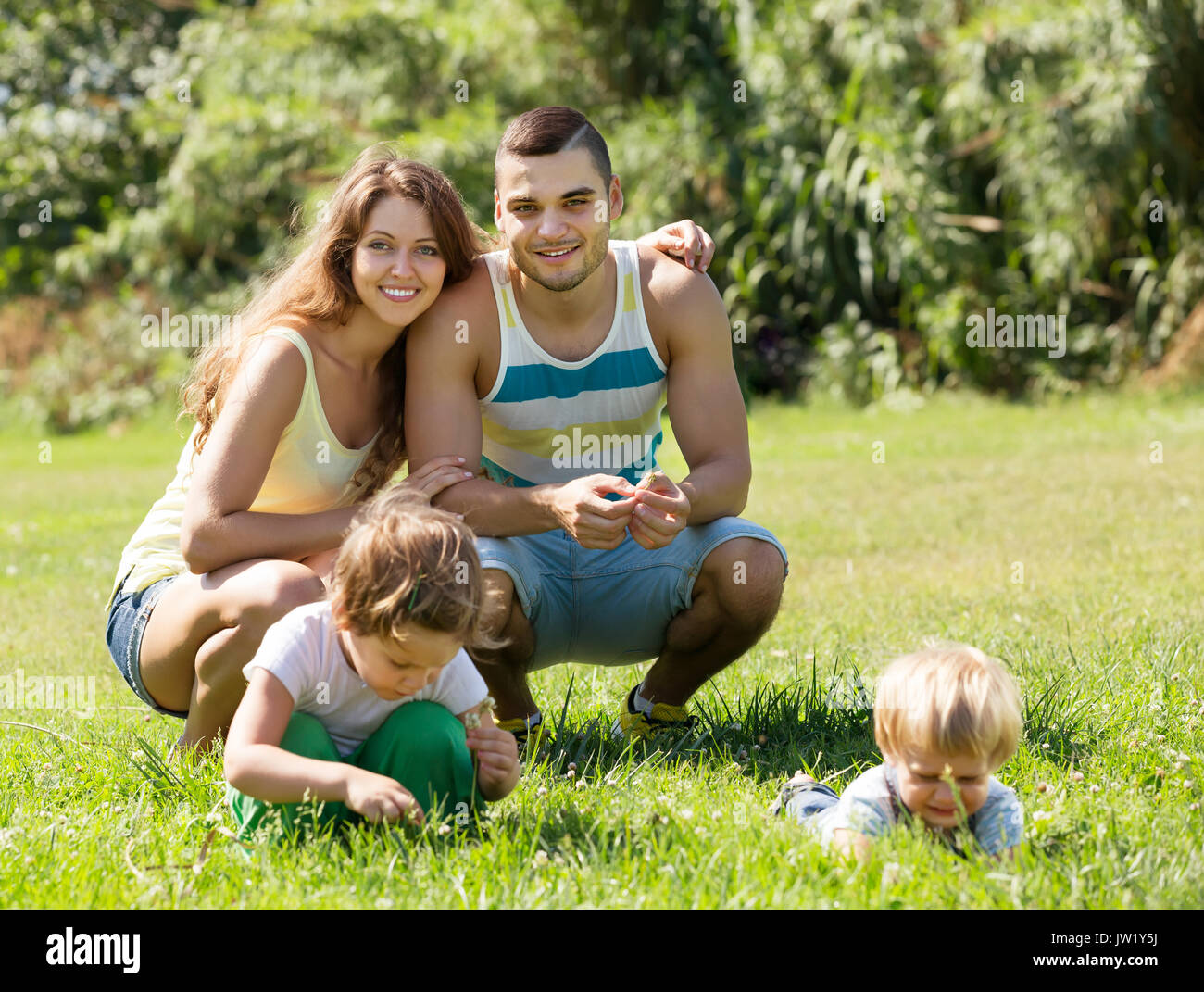 Happy smiling young famille de quatre personnes se reposant dans sunny summer park Banque D'Images