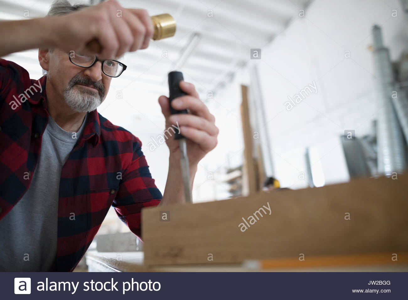 Male carpenter tapping outil ciseau sur bloc de bois à l'établi dans l'atelier Banque D'Images