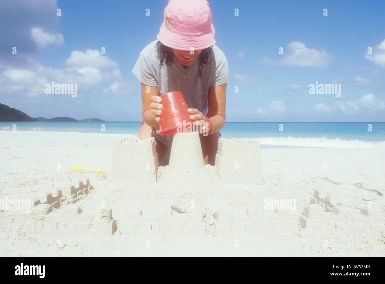 USA, USVI, St John, mature woman in pink sun hat décisions sandcastle on beach Banque D'Images