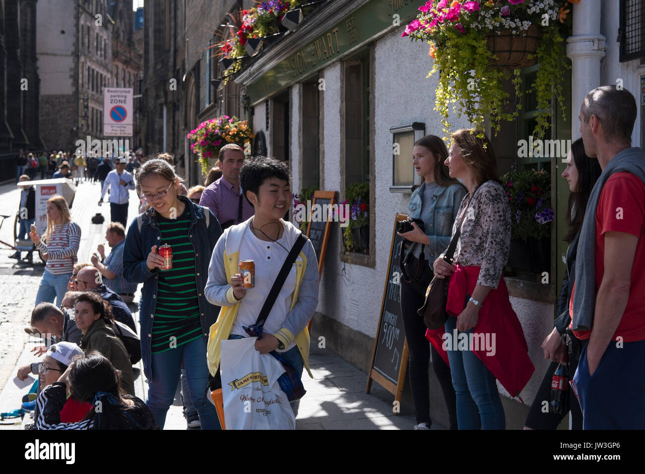 Les jeunes touristes sur une journée ensoleillée jouissant de la Royal Mile d'Édimbourg, en Écosse. Un restaurant avec des fleurs colorées est sur l'arrière-plan. Banque D'Images