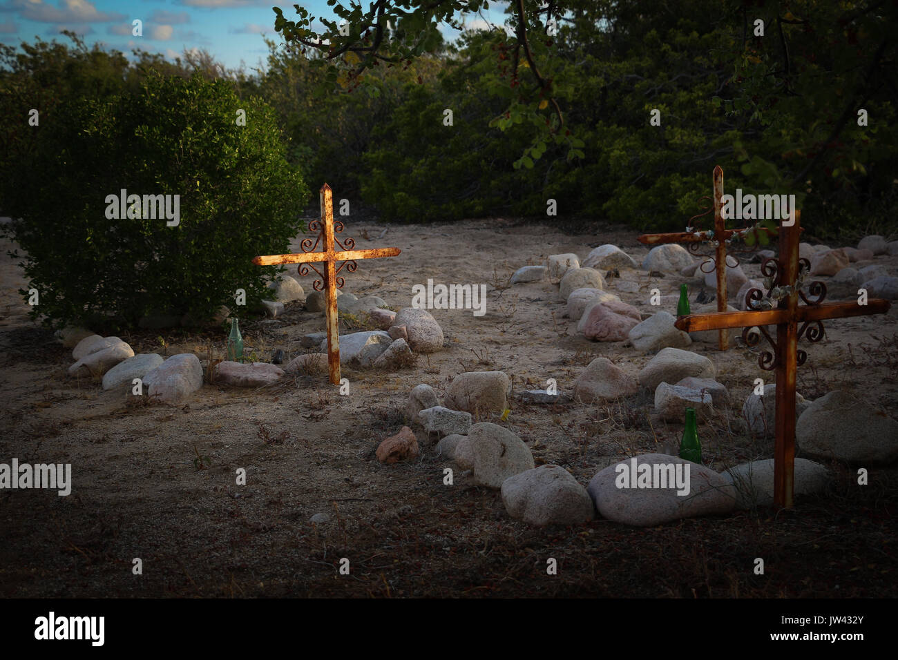 Trois tombes, décrites avec des pierres, dans une plage de arroyo dans Baja California Sur, au Mexique, avec le soleil du soir frappant une croix, le reste dans l'obscurité. Banque D'Images