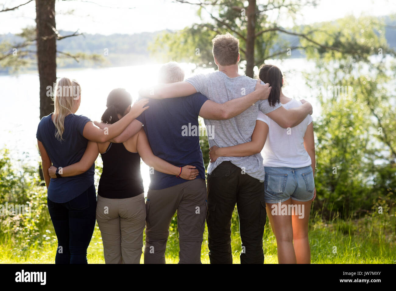 Vue arrière de l'homme et de la femme debout les bras autour d'amis sur sunny day in forest Banque D'Images
