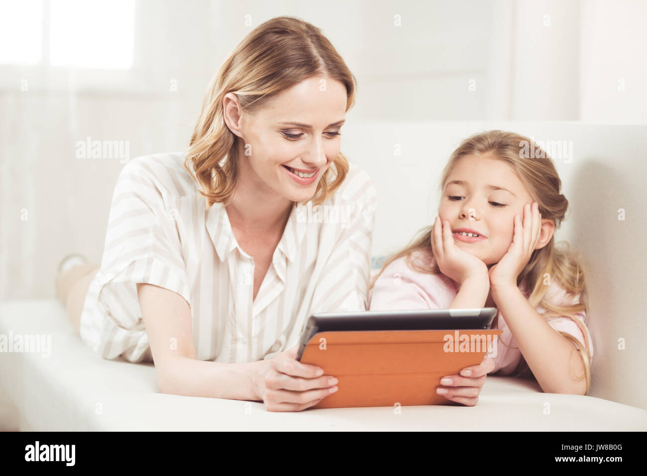 Smiling mother and daughter using digital tablet while sitting on sofa at home Banque D'Images