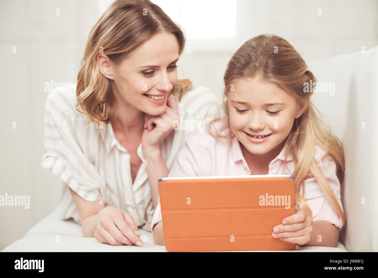 Caucasian mother and daughter using digital tablet while sitting on sofa at home Banque D'Images
