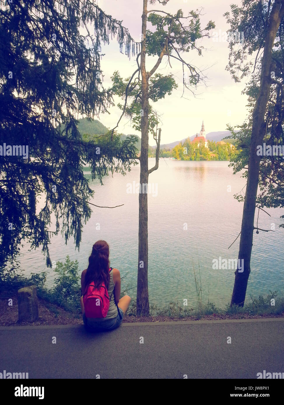 Les jeunes femmes assis sur la rive du lac de Bled à côté d'arbres avec vue sur l'église de Banque D'Images