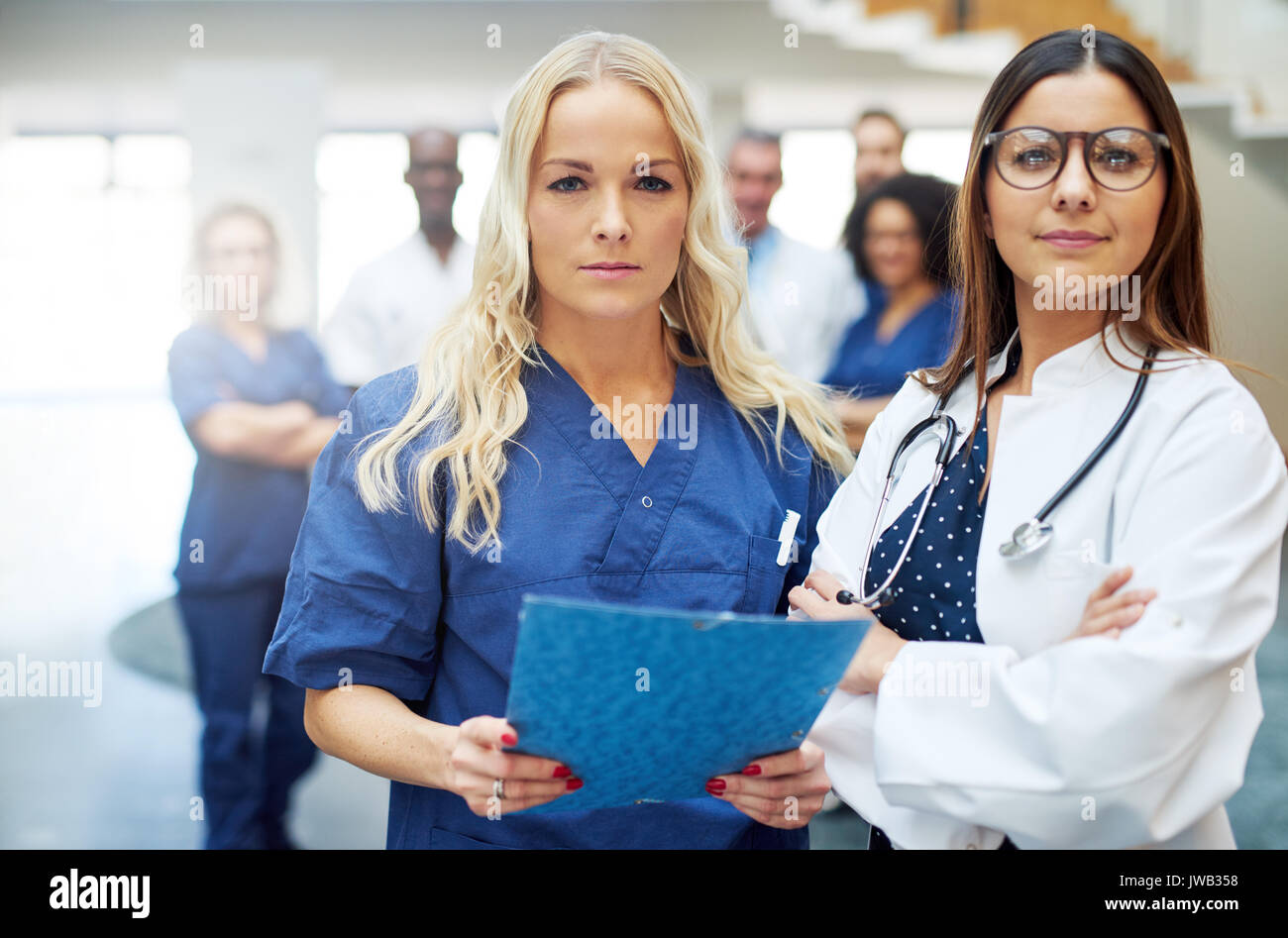 Deux jeunes femmes médecins looking at camera debout dans un hôpital avec les papiers. Banque D'Images