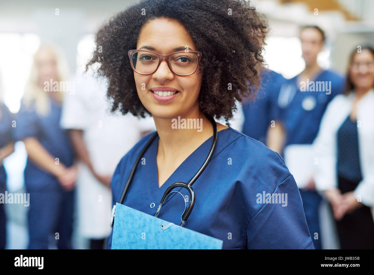 Jeune femme noire doctor looking at camera dans un hôpital en face de l'équipe médicale Banque D'Images