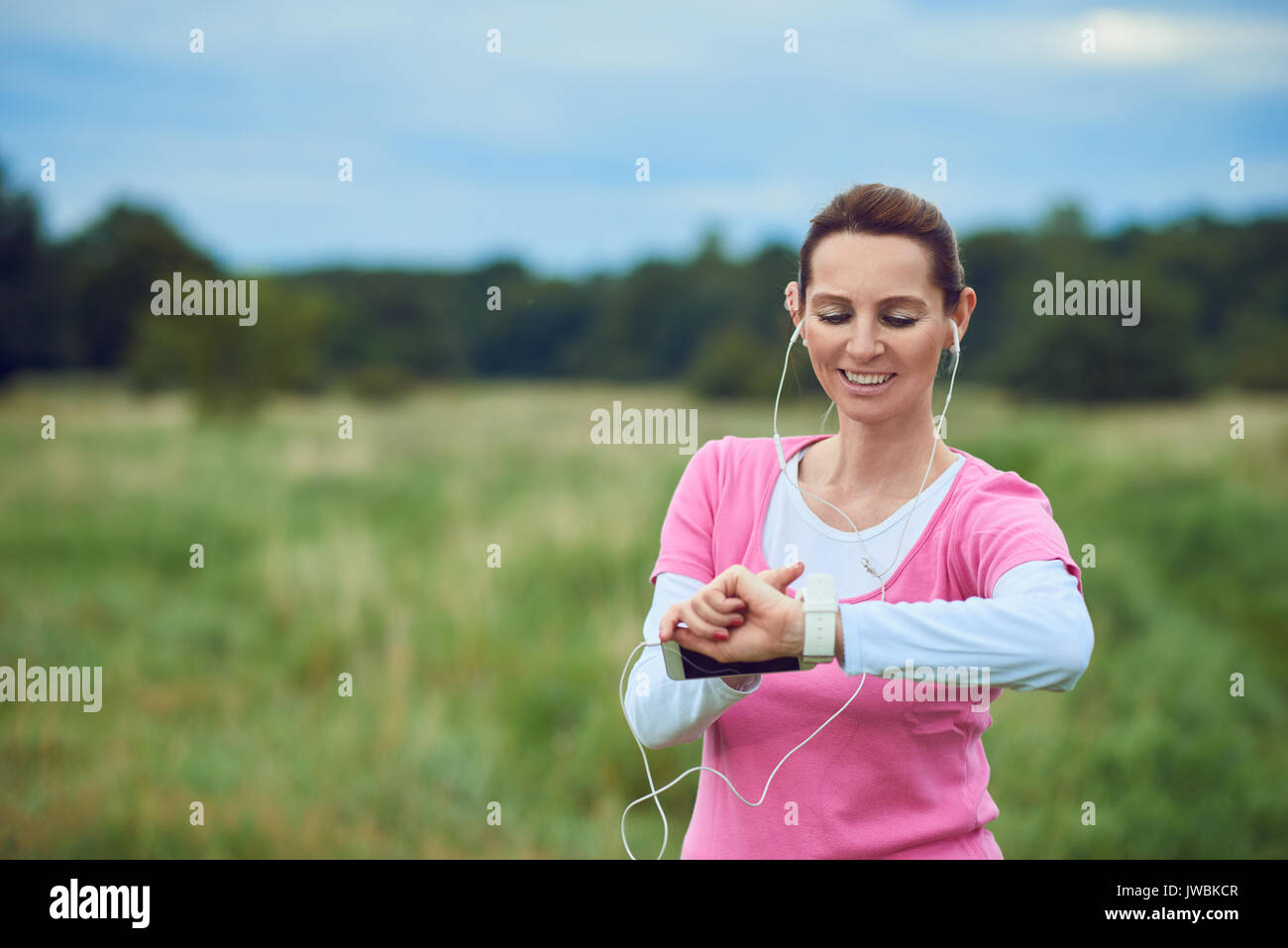 Femme d'âge moyen contrôler son sport ou de la santé regarder tandis que dehors le jogging dans la campagne à l'écoute de la musique sur son téléphone mobile dans une saine lifestyl Banque D'Images