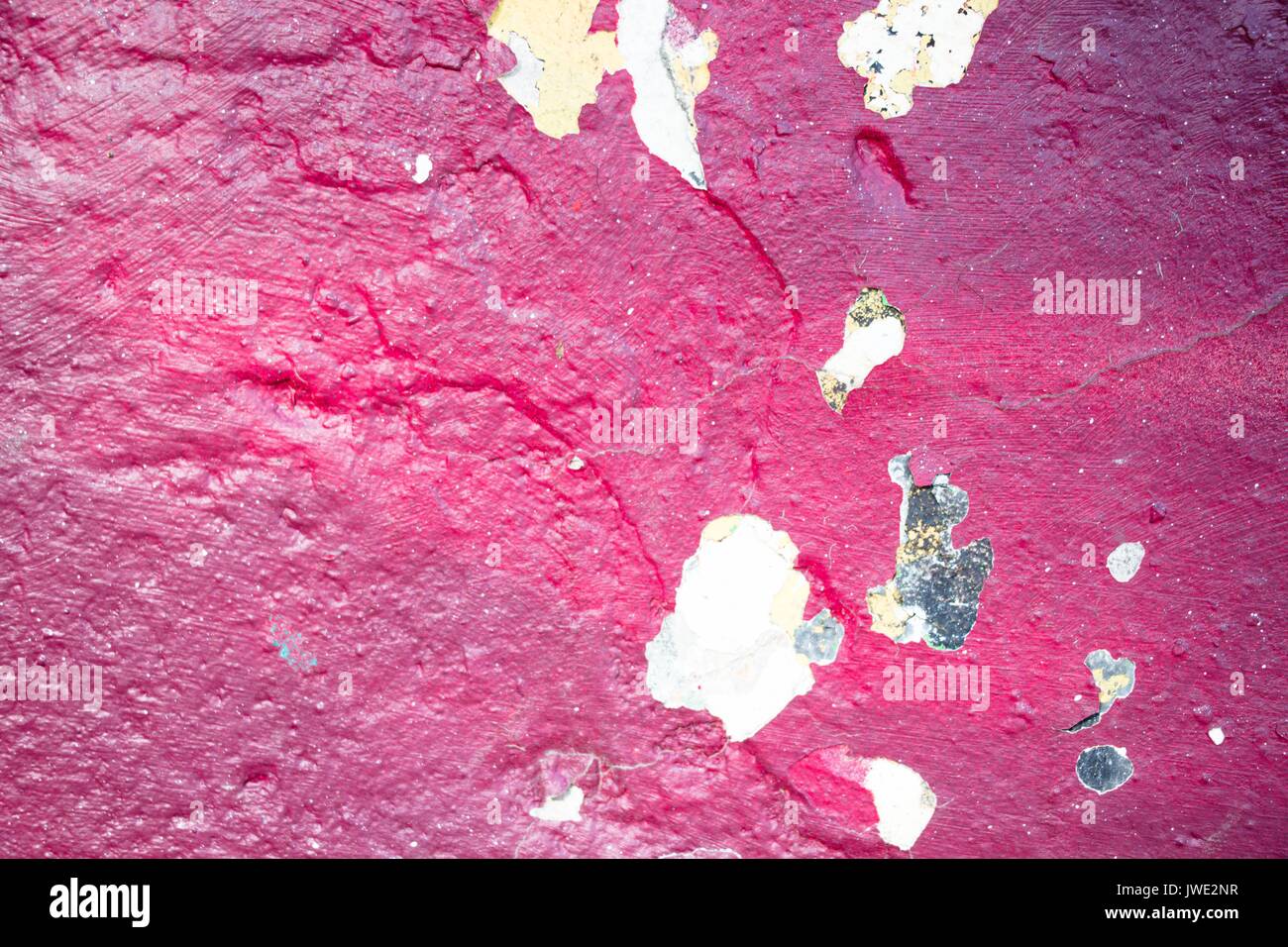 La texture d'une peinture craquelée de nuance rouge sur un mur de béton Banque D'Images