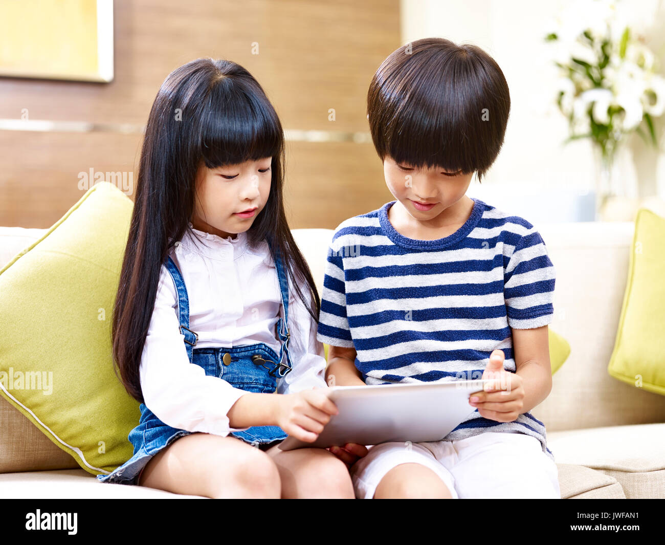 Deux frère et sœur asiatique assis sur table à l'aide d'accueil looking at digital tablet. Banque D'Images