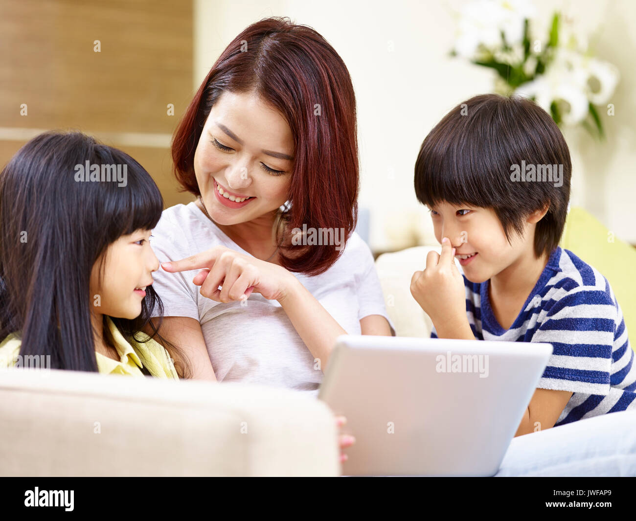 Young woman sitting on sofa at home s'amusant à jouer avec son fils et sa fille. Banque D'Images