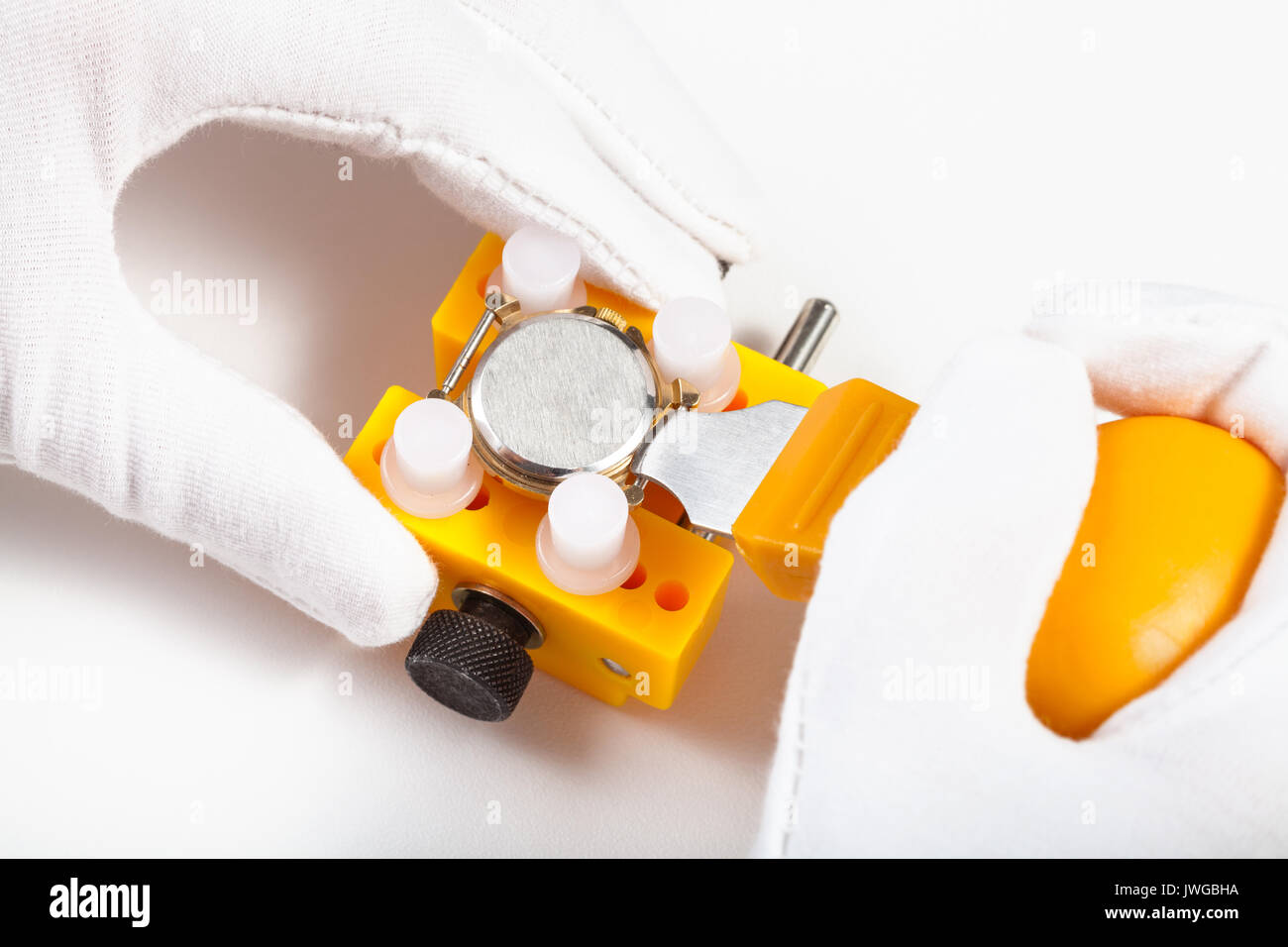 Atelier horloger - retirer le couvercle arrière de la montre pour remplacer la batterie par l'ouvreur jaune sur fond blanc Banque D'Images