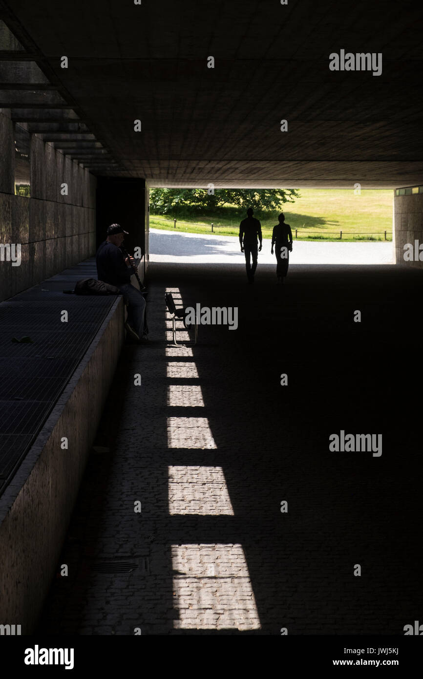 Un musicien ambulant joue du saxophone dans l'ombre d'un passage inférieur pour piétons entre l'Englischer Garten, jardin anglais, et le Dichter garten, Munich, Bavaria, Germany Banque D'Images