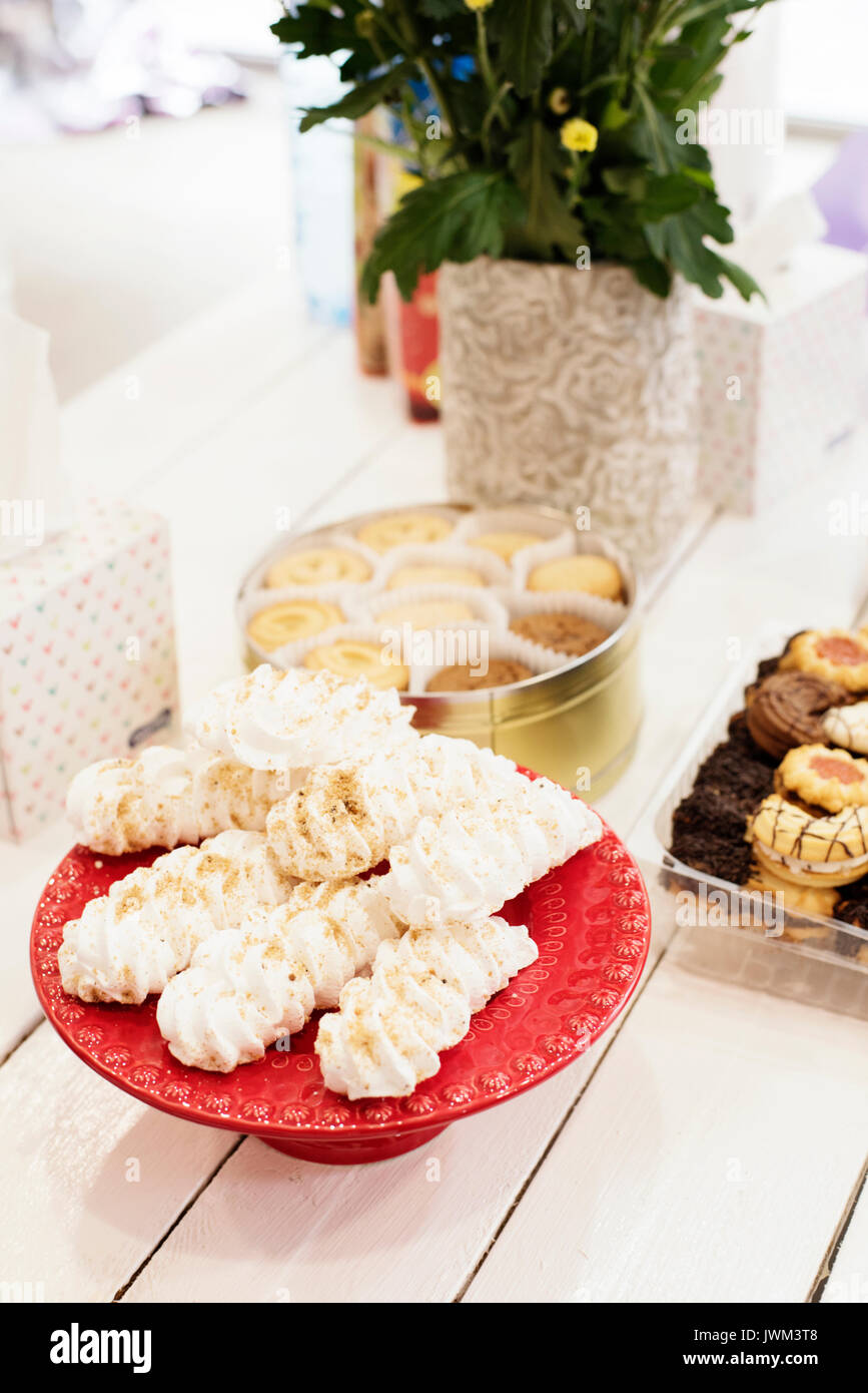 Candy bar Table avec des sucreries, bonbons, dessert. Meringue française cookies en rouge haut plateau, bac. Le blanc d'Oeuf bonbons, biscuits et fleurs sur fond blanc ne Banque D'Images