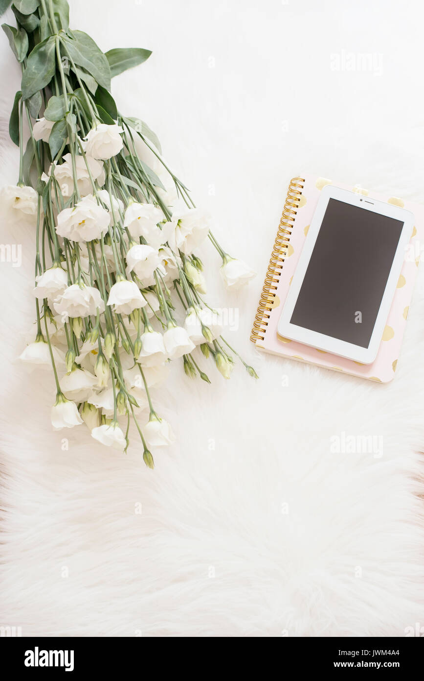 Portable, tablette et un gros bouquet de fleurs blanches sur le sol sur un tapis de fourrure blanche. La mode et la féminité dans l'espace confortable accueil Télévision Banque D'Images