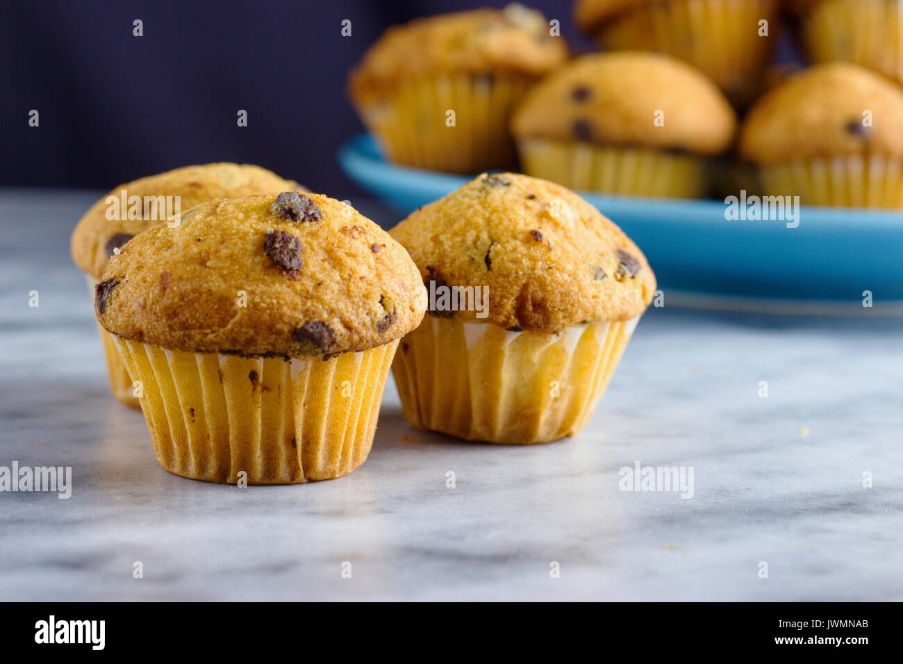 Mini muffins aux pépites de chocolat sur la surface en marbre en face de la plaque bleue avec un peu plus de muffins Banque D'Images