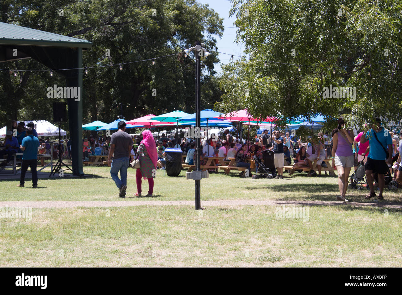 Beaucoup de gens assis sous parasols colorés à l'extérieur à l'Austin Ice Cream Festival. Couple indien passé marche avec écharpe rose vif. Banque D'Images