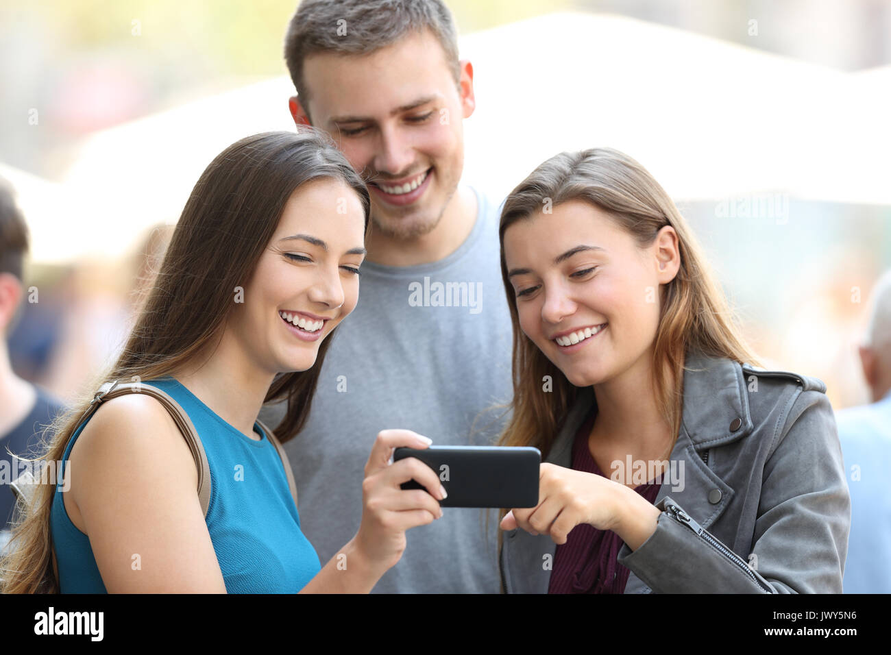 Trois amis heureux le partage de contenu multimédia avec un téléphone intelligent dans la rue Banque D'Images