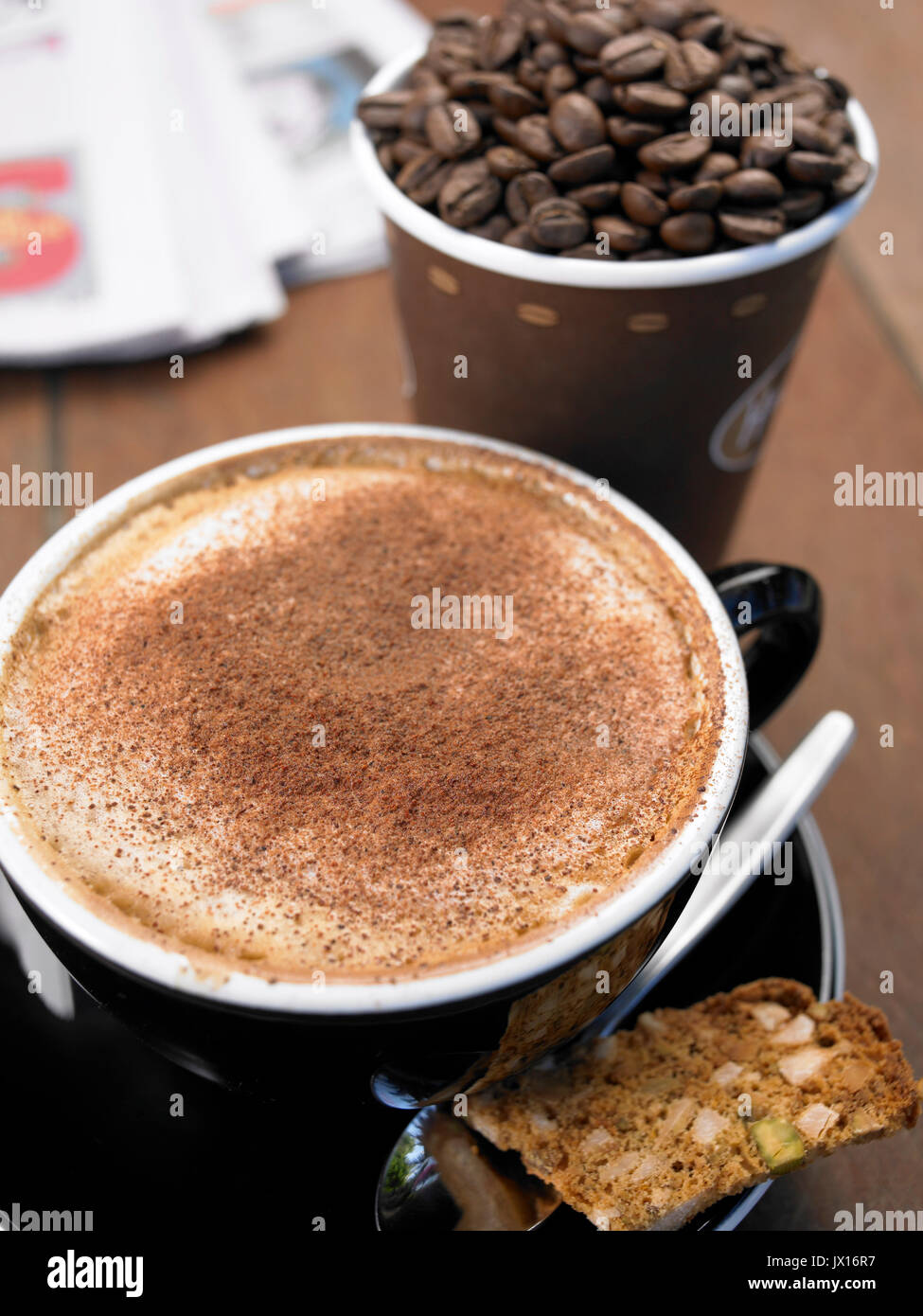 Cappuccino avec de la cannelle avec vente à emporter tasse pleine de haricots ,Journal et biscotti Banque D'Images